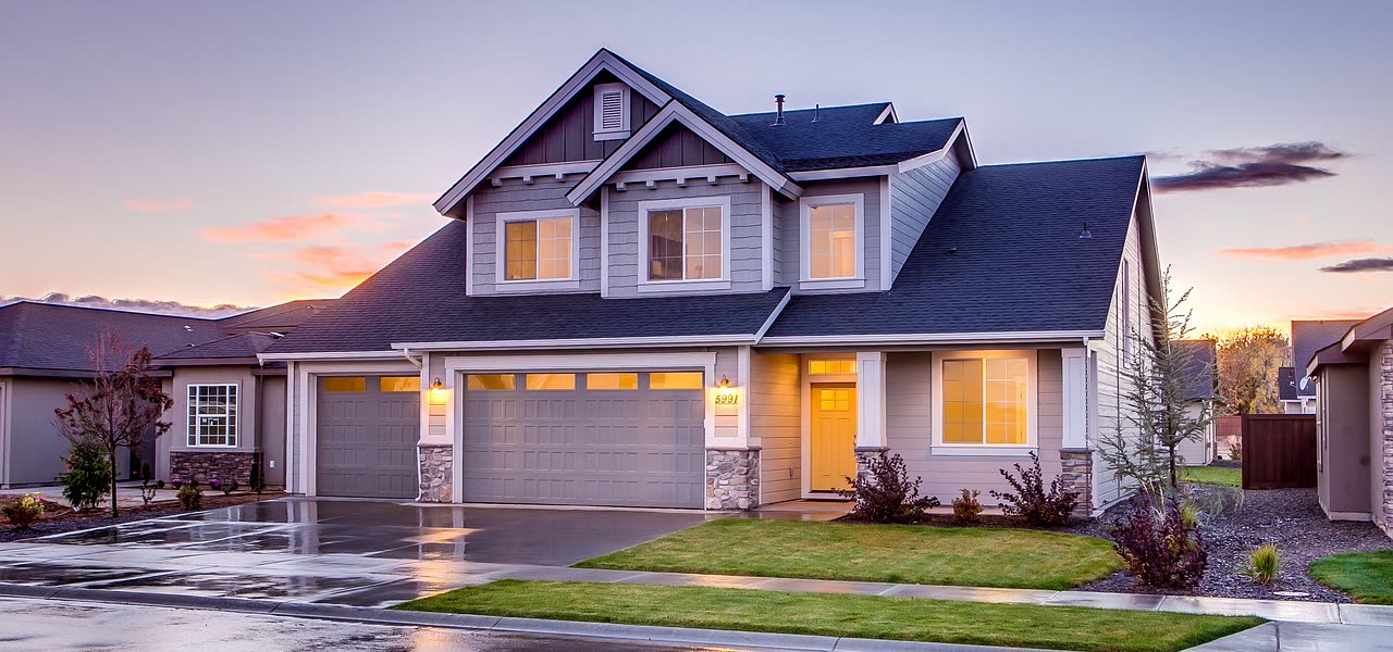 A suburban home at dusk, warm lights on after the rain